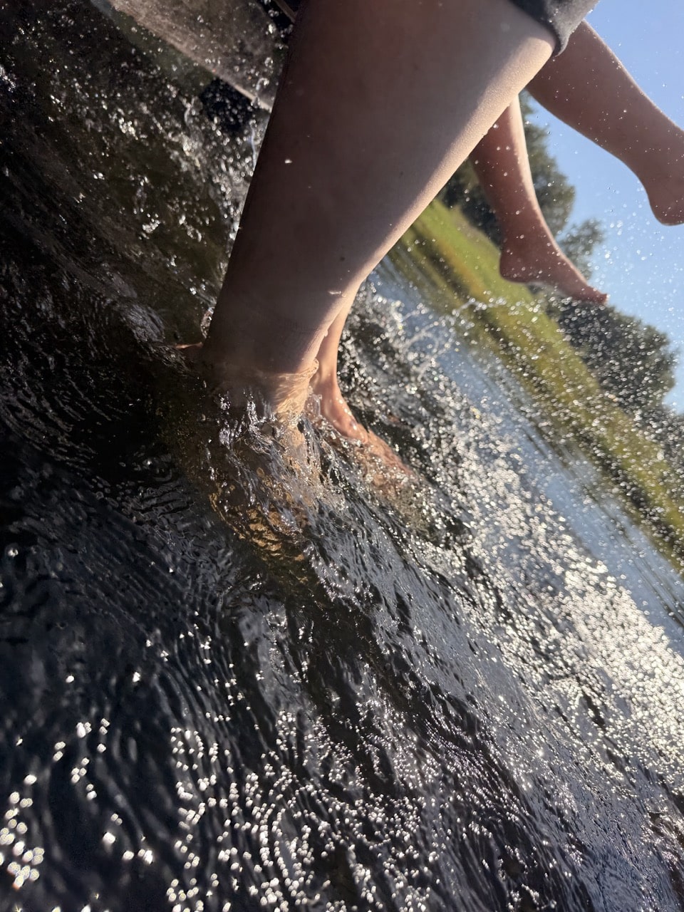 Füße im klaren dunklen Wasser des Badeweihers in Mauth
